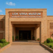 Front view of Lok Virsa Museum in Islamabad showing its sandstone architecture, large entrance archway, carved decorative panels, green lawns, and clear blue sky.